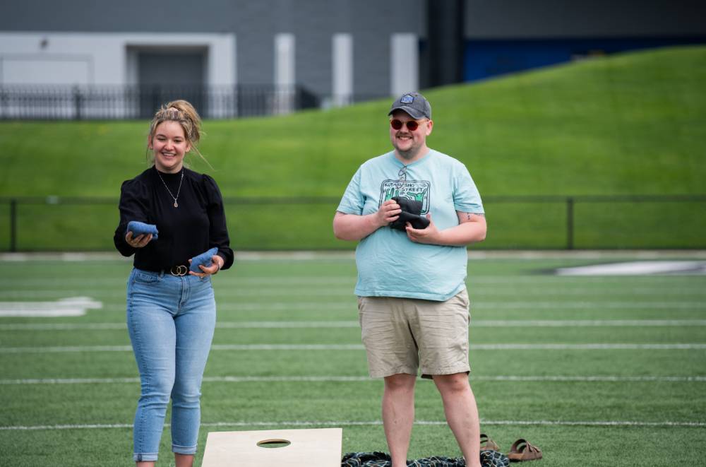 Zach Jacobs and Michele Renaud smiling together next to a cornhole board